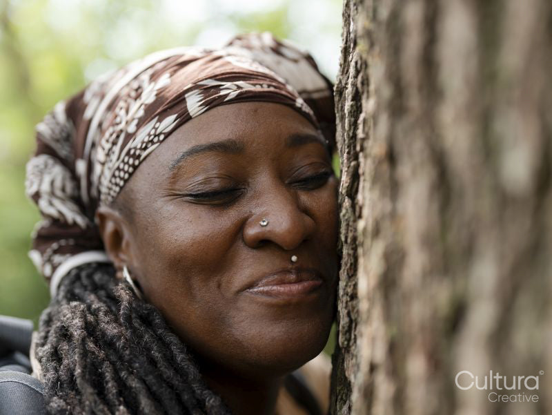 Smiling mature woman hugging tree in forest
