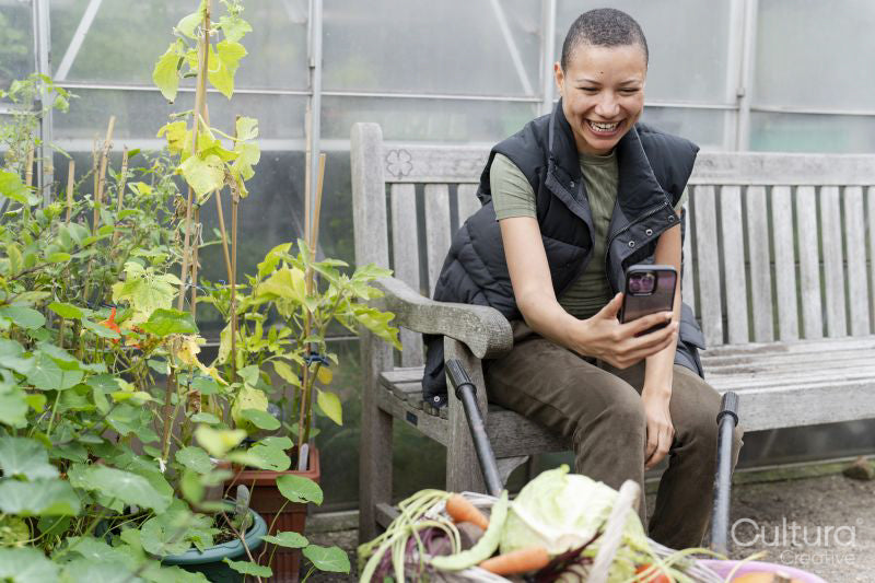 Smiling woman photographing harvested vegetables with smart phone