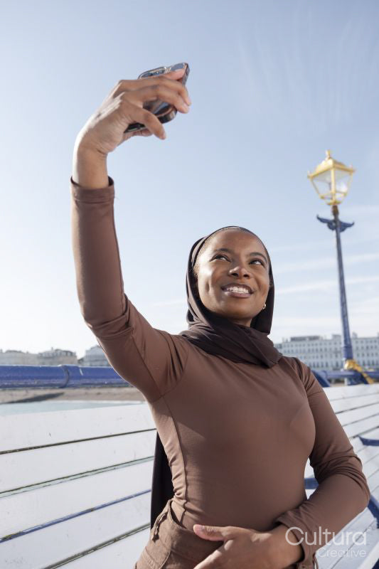 Muslim woman taking selfie while standing on pier on sunny day