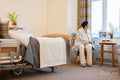 Senior lady sitting and looking through window in bedroom at nursing home