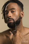 Studio portrait of young man with dreadlocks trimming beard