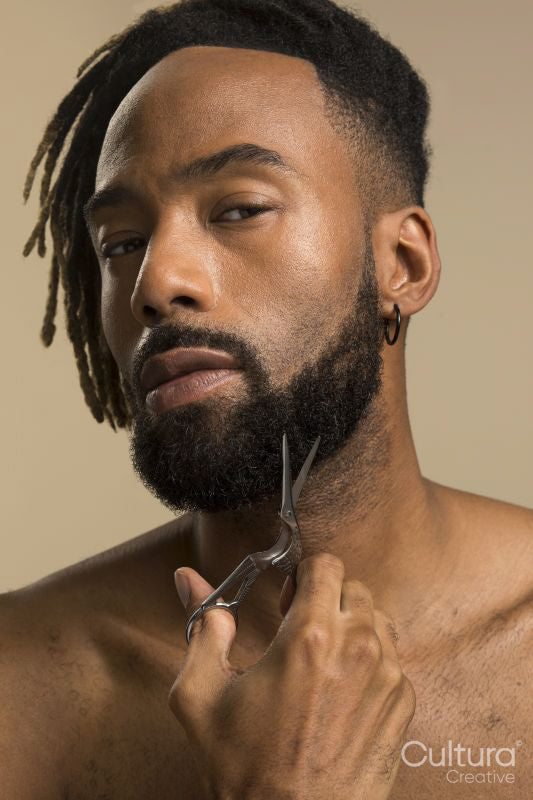Studio portrait of young man with dreadlocks trimming beard