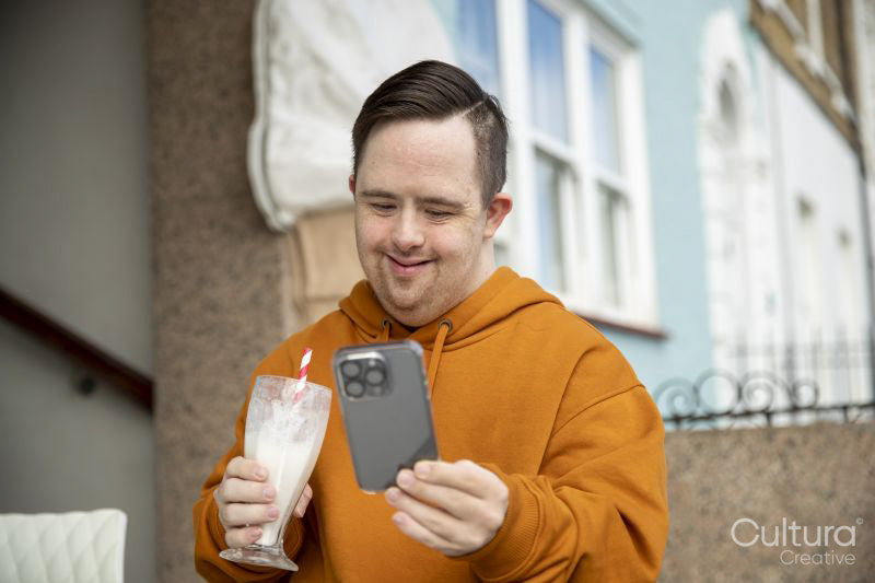 Man in sidewalk cafe drinking milkshake and using phone