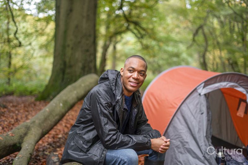 Smiling man sitting next to tent in forest