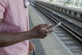 Close up of man holding smart phone while standing on railway platform