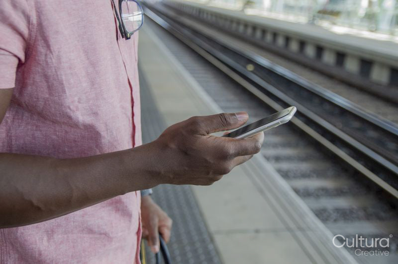 Close up of man holding smart phone while standing on railway platform