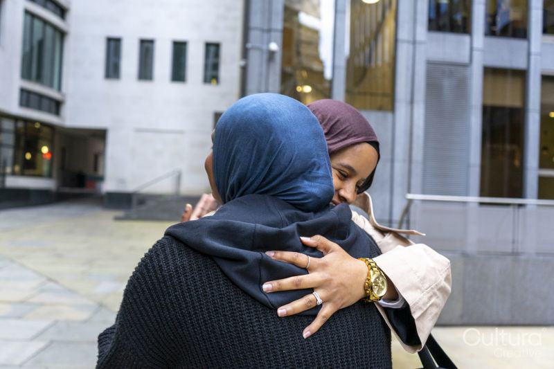 Two women wearing hijabs hugging in street