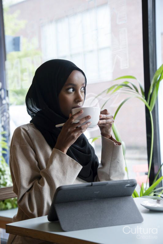 Young woman in hijab working on tablet in cafe