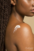 Clopse-up of shirtless woman with braided hair and body lotion on shoulder