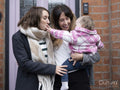 Two women standing at doorstep and holding baby