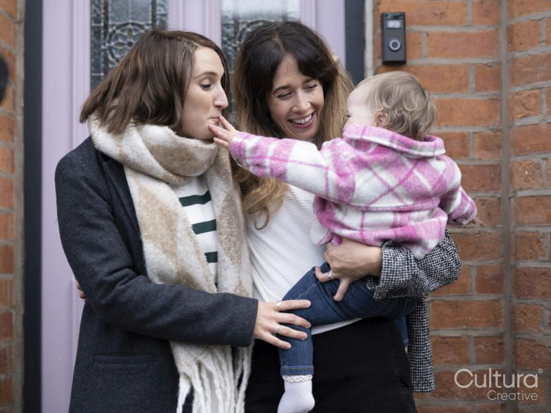 Two women standing at doorstep and holding baby