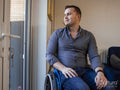 Man sitting on wheelchair at home, looking through window