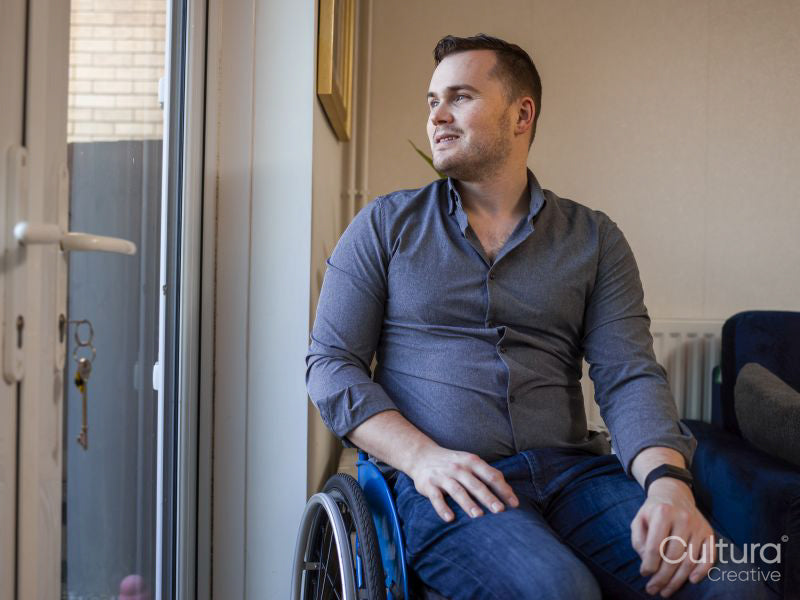 Man sitting on wheelchair at home, looking through window