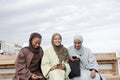 Three Muslin women using smart phones while sitting on bench