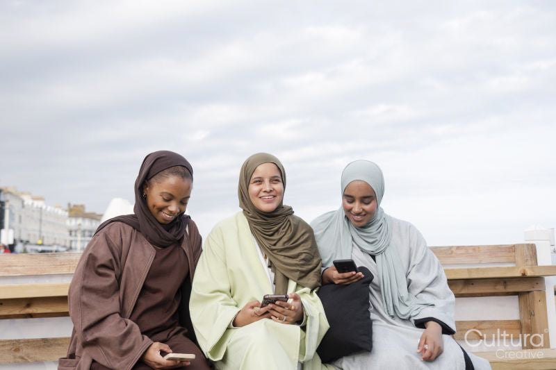 Three Muslin women using smart phones while sitting on bench