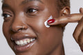 Close-up of smiling woman applying face cream on cheek