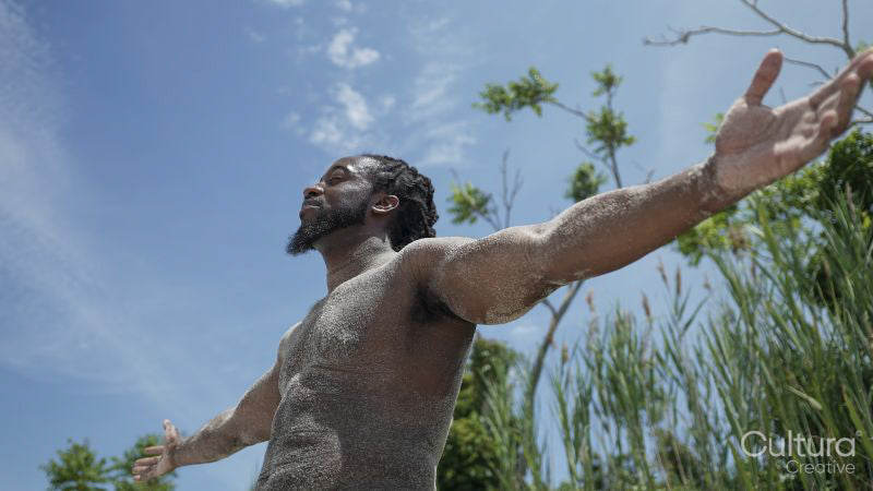 Shirtless man covered with sand standing on beach with arms outstretched