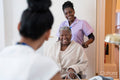 Smiling female nurse with senior woman sitting in wheelchair entering doctors office