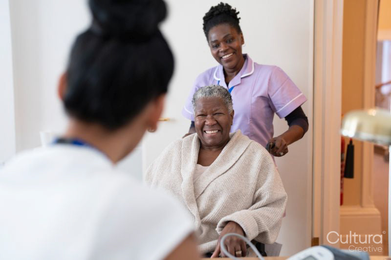 Smiling female nurse with senior woman sitting in wheelchair entering doctors office