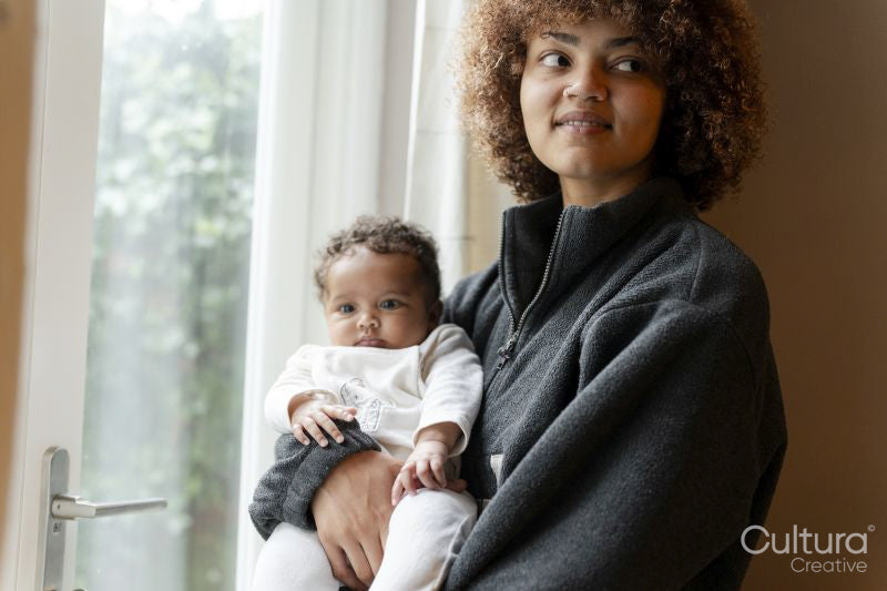Mother holding baby daughter next to window