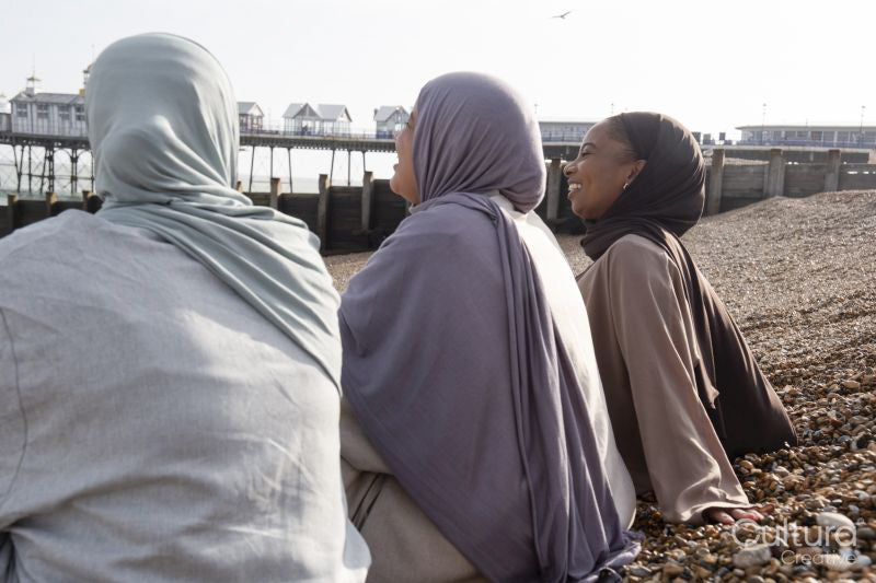 Three Muslim women sitting on beach on sunny day