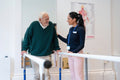 Female therapist assisting senior man walking on bars in exercise room