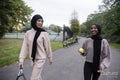 Two women in hijabs walking in park with tennis racket and ball