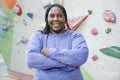 Portrait of smiling woman standing with arms crossed in front of climbing wall