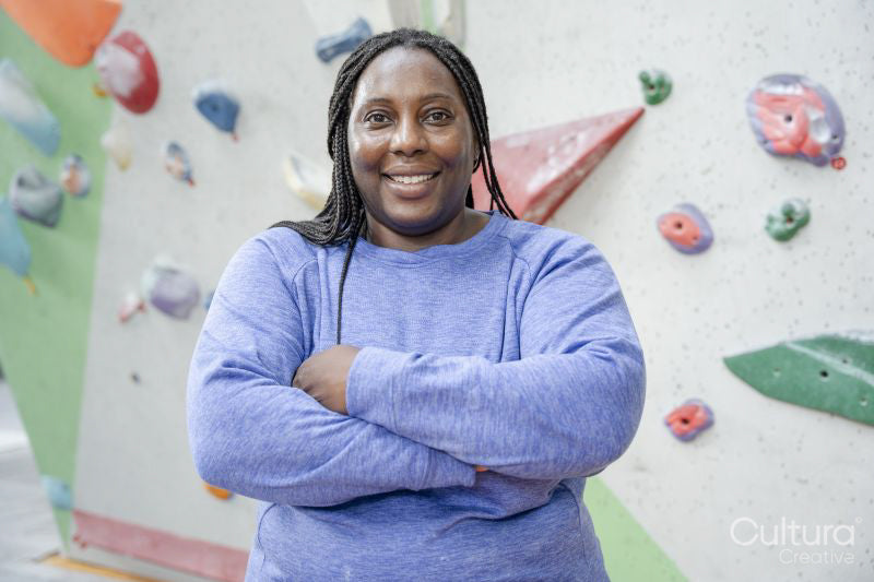 Portrait of smiling woman standing with arms crossed in front of climbing wall