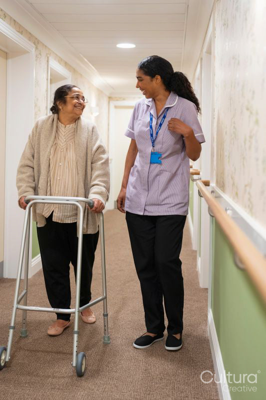 Nurse helping senior lady to walk with mobility walker at nursing home