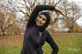 Smiling woman in black sports clothing and hijab stretching in park