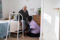 Caregiver helping senior man sitting on bed to put on shoes