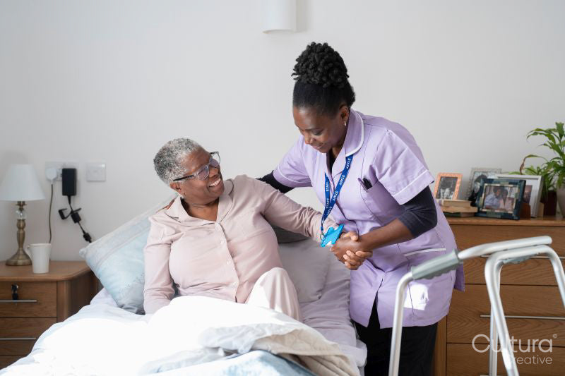 Caregiver assisting smiling senior woman sitting on bed