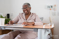 Smiling senior woman in bathrobe sitting on bed and doing crossword puzzle in nursing home