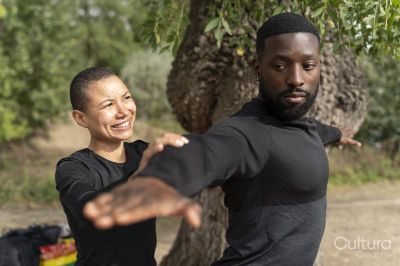 Yoga instructor assisting man practicing yoga in park