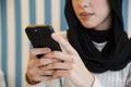 Young woman in hijab using phone in cafe