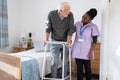 Smiling caregiver assisting senior man standing with mobility walker