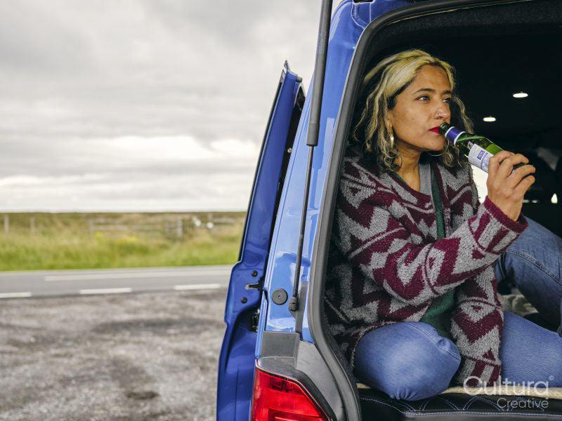 Woman sitting in back of van and drinking beer