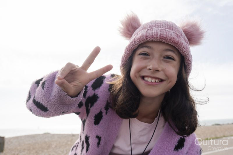 Portrait of smiling girl making peace gesture on beach on cloudy day