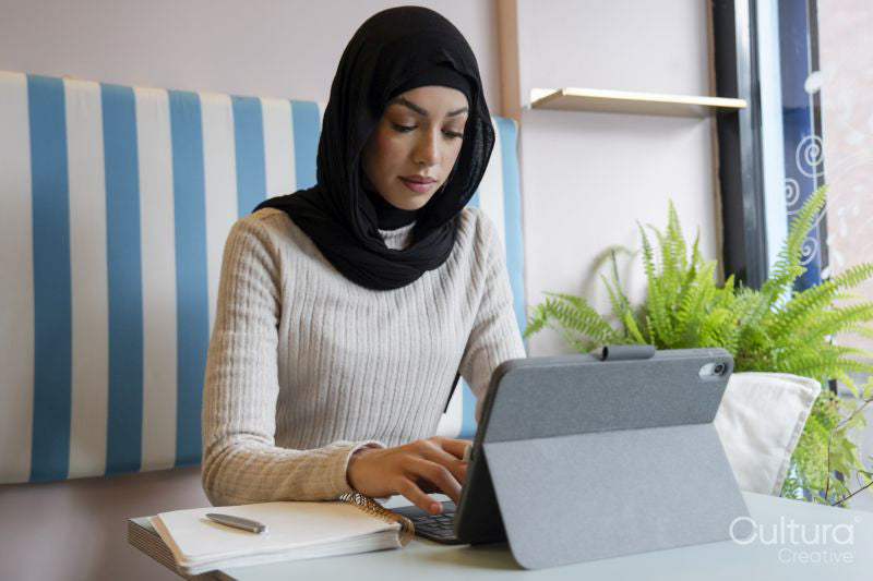 Young woman in hijab working on tablet in cafe
