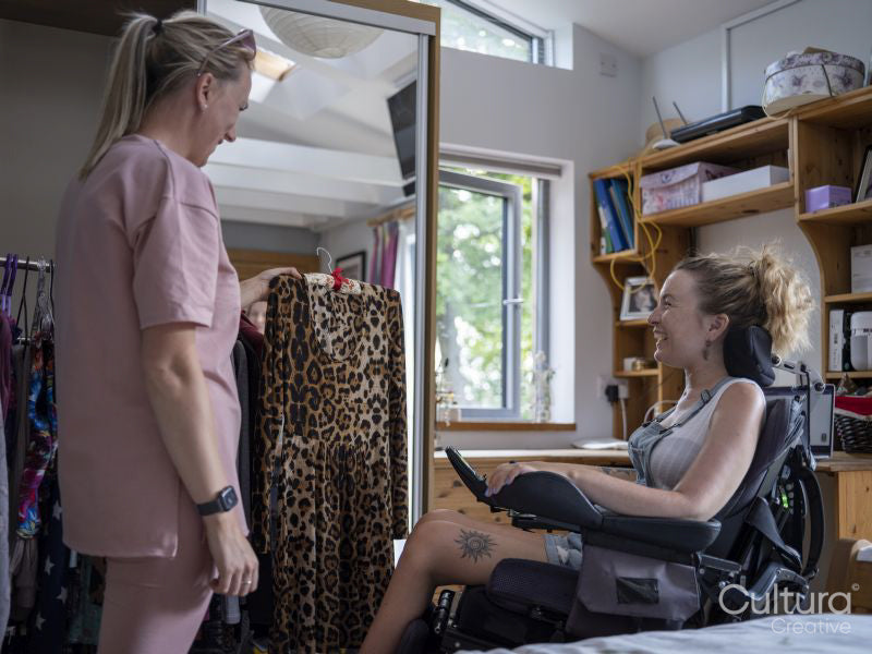 Assistant helping woman in wheelchair pick clothes