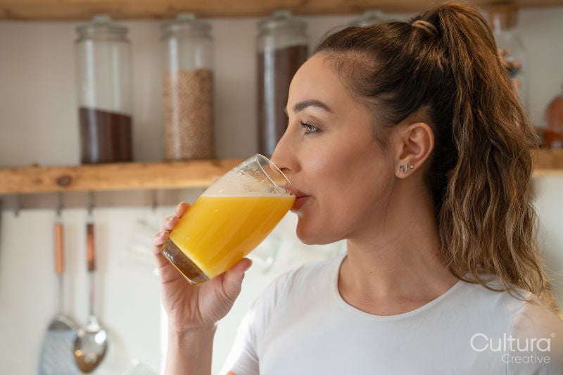 Woman in kitchen, drinking orange juice