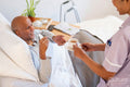 Nurse serving coffee to senior man lying in bed in room at nursing home