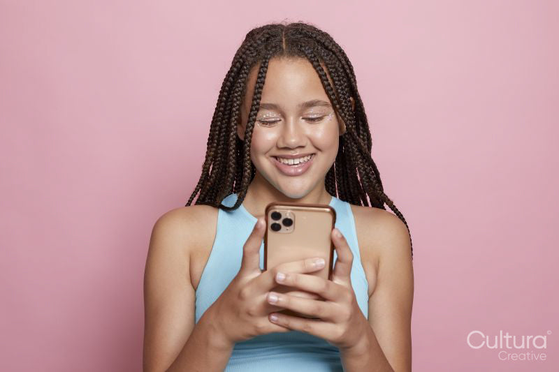Studio shot of smiling girl with braids looking at smart phone