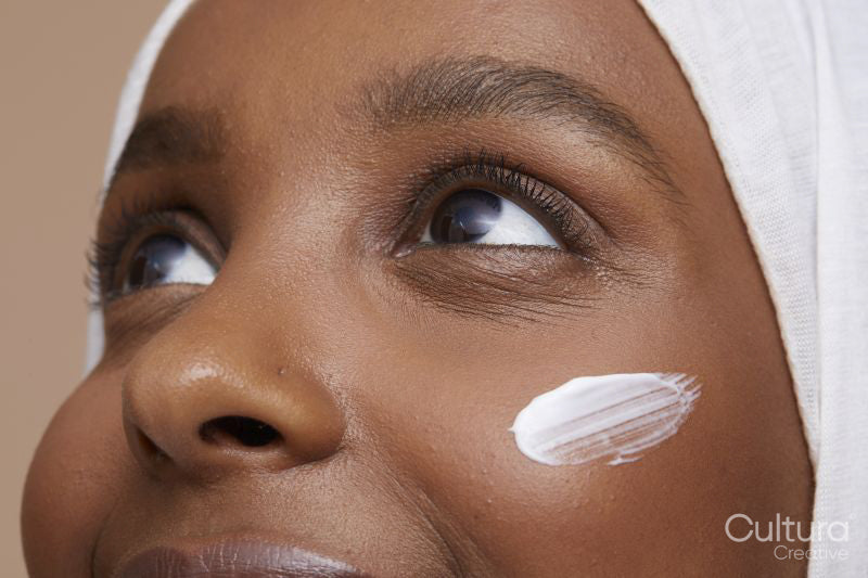 Studio shot of young woman in white hijab applying face cream