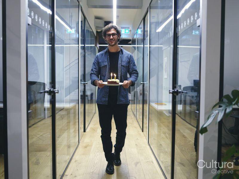 Smiling man carrying birthday cake in corridor in modern office