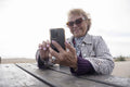 Senior woman using smart phone while sitting by picnic table on beach