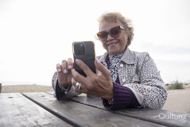 Senior woman using smart phone while sitting by picnic table on beach