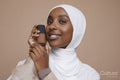 Studio portrait of young woman in white hijab holding foundation bottle