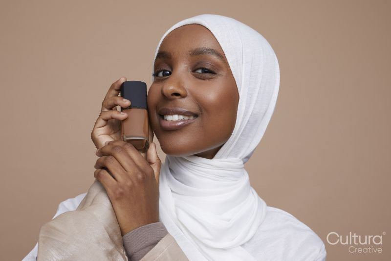 Studio portrait of young woman in white hijab holding foundation bottle